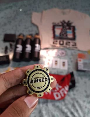 An MLH winner pin held in front of hackathon prizes and merchandise